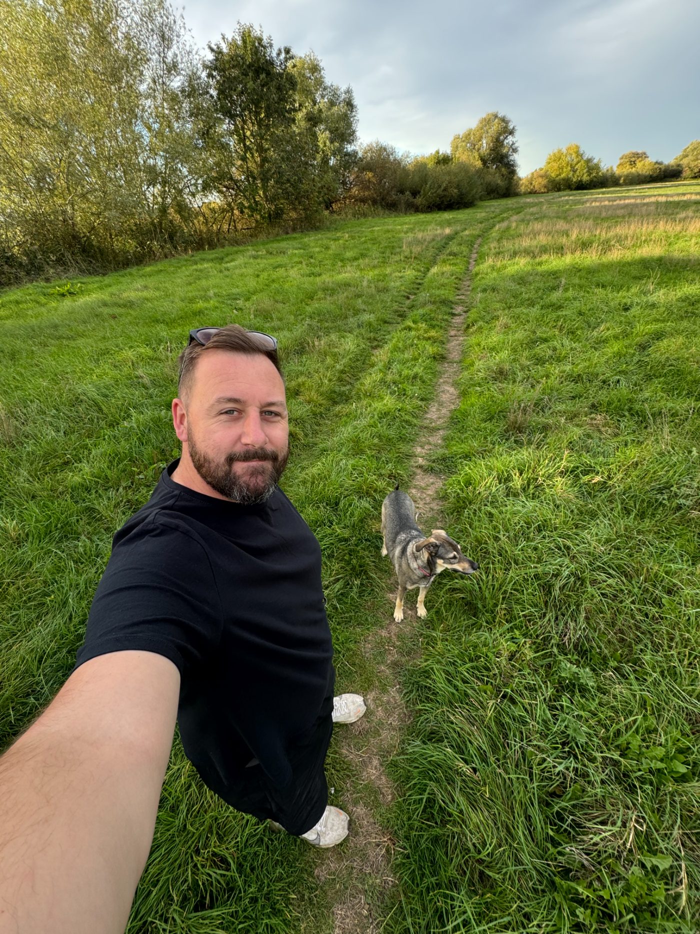 Mark taking a selfie in a field with Hollie on the path behind